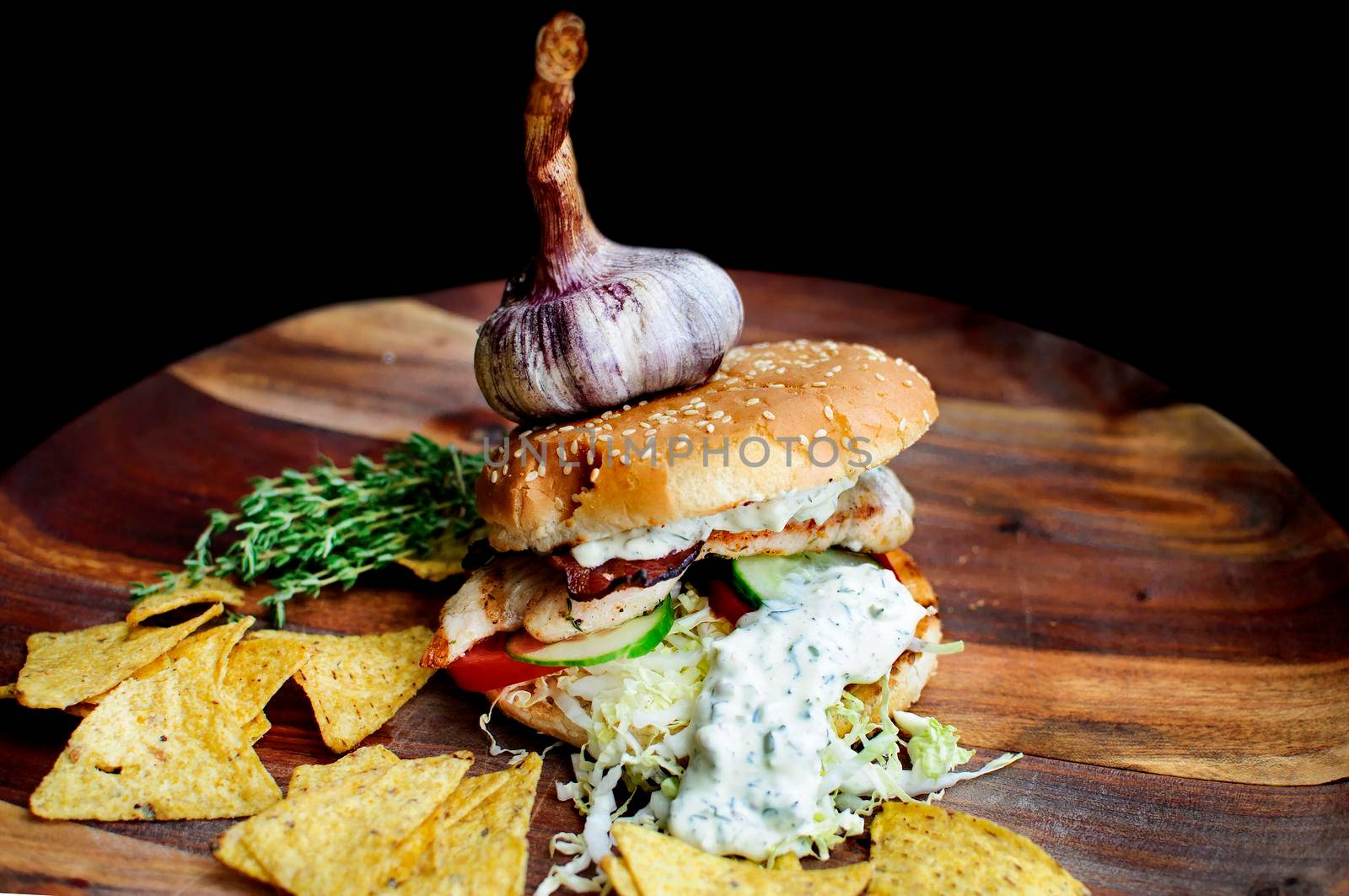 Creatively styled beef burger with rustic home-made French chips or crisps shot against a dark background with generous accommodation for copy space. garlic on top