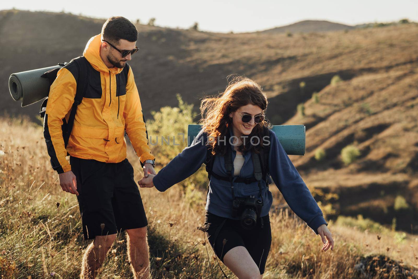 Cheerful Woman with Her Boyfriend Holding by Hands While Hiking on Hill During Sunset, Young Couple Enjoy Their Trip