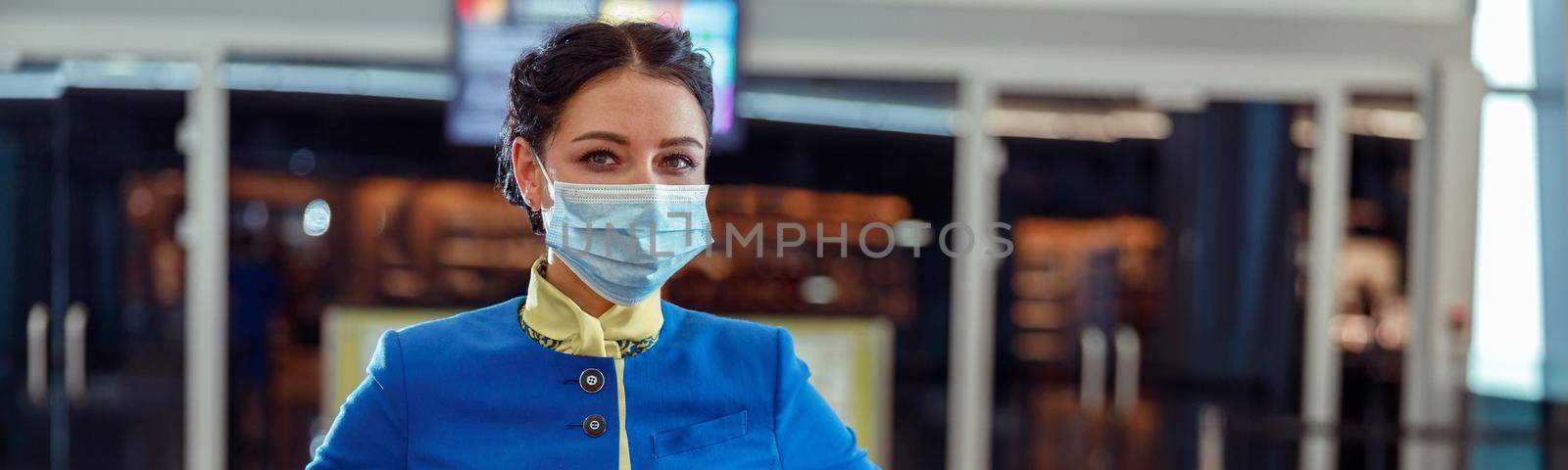 Female flight attendant wearing protective face mask and air hostess uniform while standing at airport during pandemic
