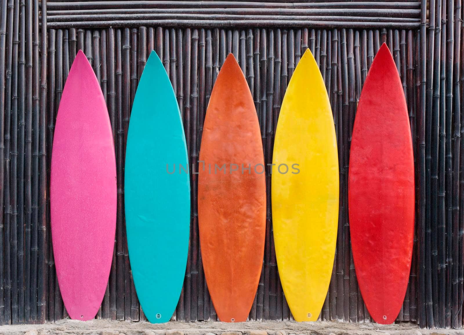 Colored surfboards leaning up against a wooden fence on beach