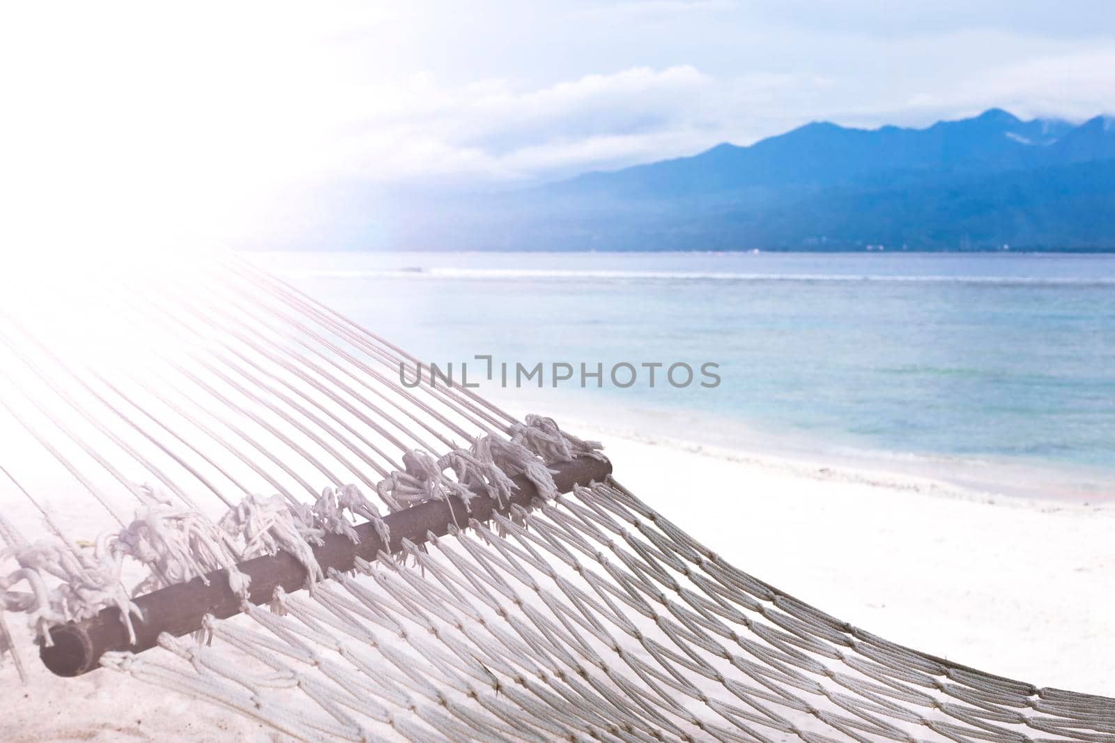 Hammock hanging between trees on a sandy beach on a background of azure Bali Sea. Coast of the Gili Trawangan island, Indonesia.