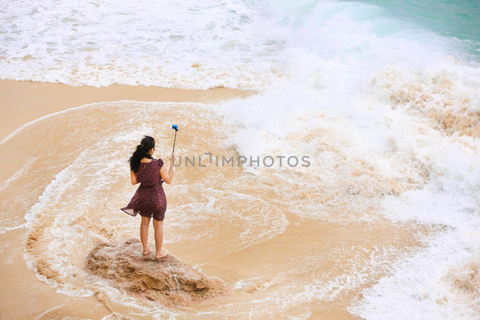 Female traveler taking selfie at the beach. Back view