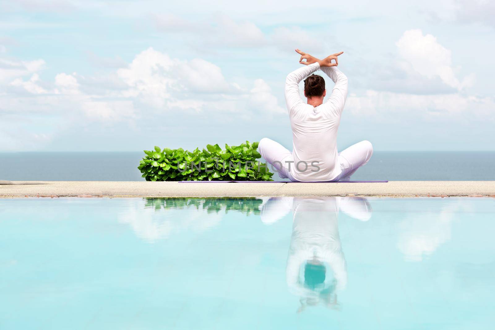 Caucasian man in white clothes meditating yoga on the sea shore pier or platform