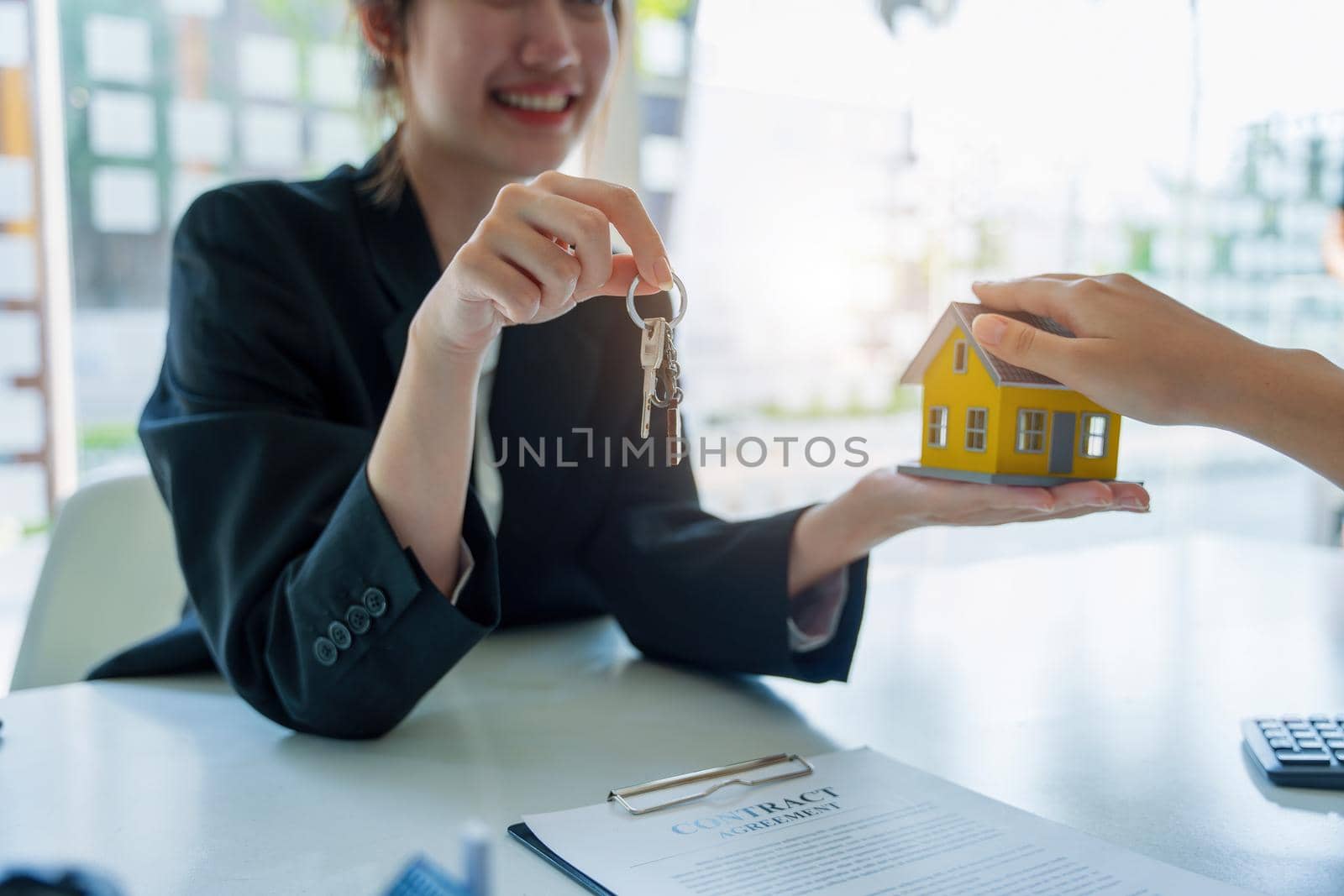 Accountant, businessman, real estate agent, Asian business woman handing keys to customers along with house after customers to sign.