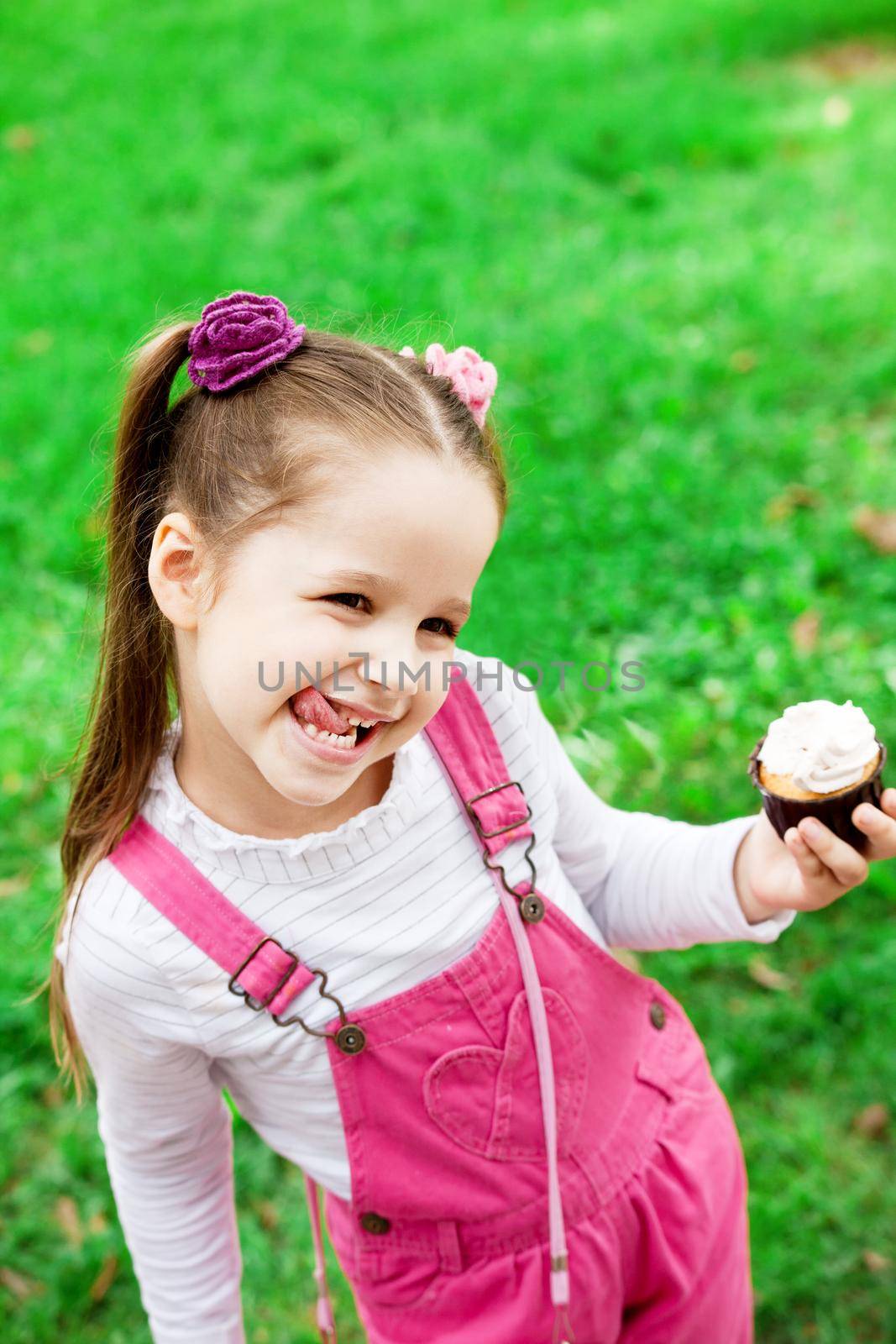 Happy little girl eating cake and having fun at the park by Jyliana