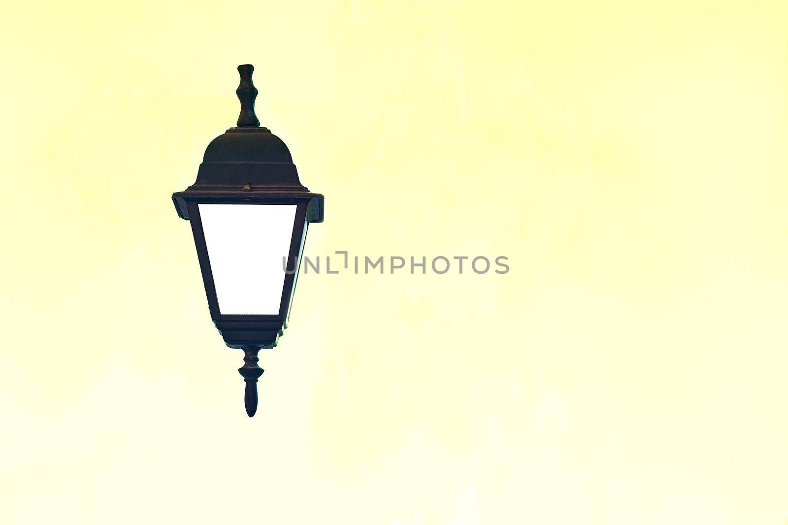 a lamp with a transparent case protecting the flame or electric bulb, and typically having a handle by which it can be carried or hung. Antique black lantern on a pale yellow background