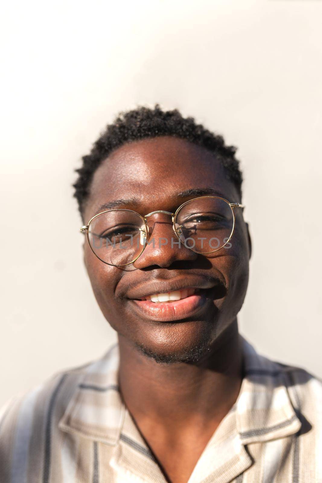 Vertical headshot of young happy and smiling black man wearing glasses outdoors. by Hoverstock