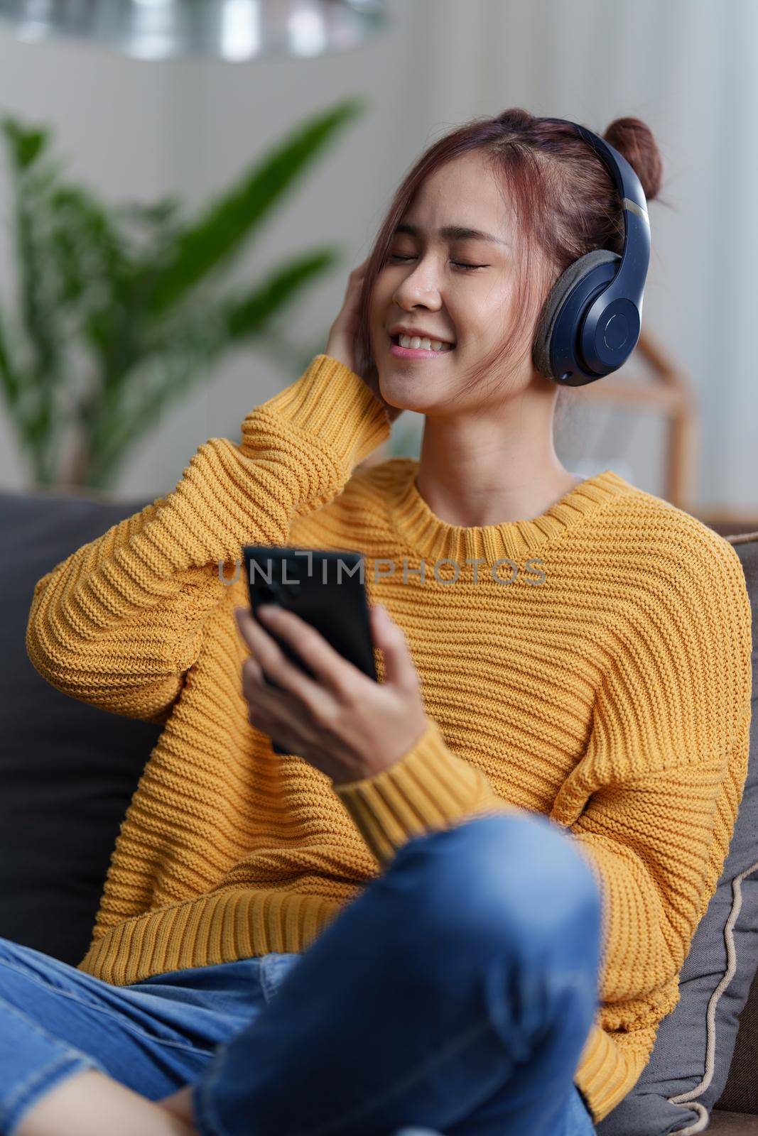 Portrait of Asian woman sitting at sofa and listening to music on phone at home by phone