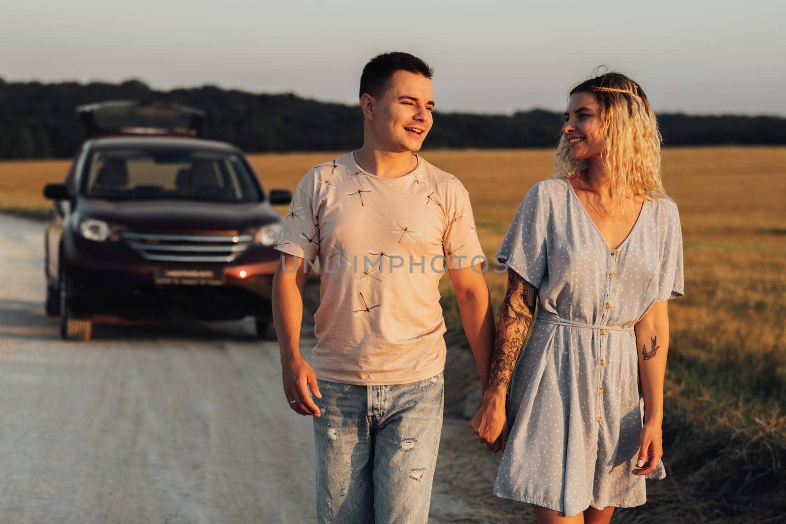 Caucasian Man and Woman Holding by Hands on the Background of Their SUV Car, Young Couple Enjoying Road Trip at Sunset by Romvy