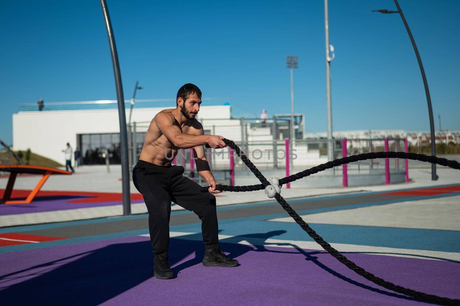 Shirtless man doing exercises with ropes outdoors