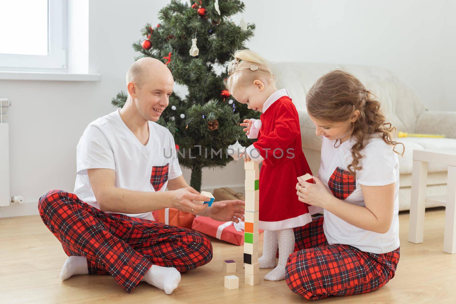 Toddler child with cochlear implant plays with parents under christmas tree - deafness and innovating medical technologies for hearing aid and diversity by Satura86