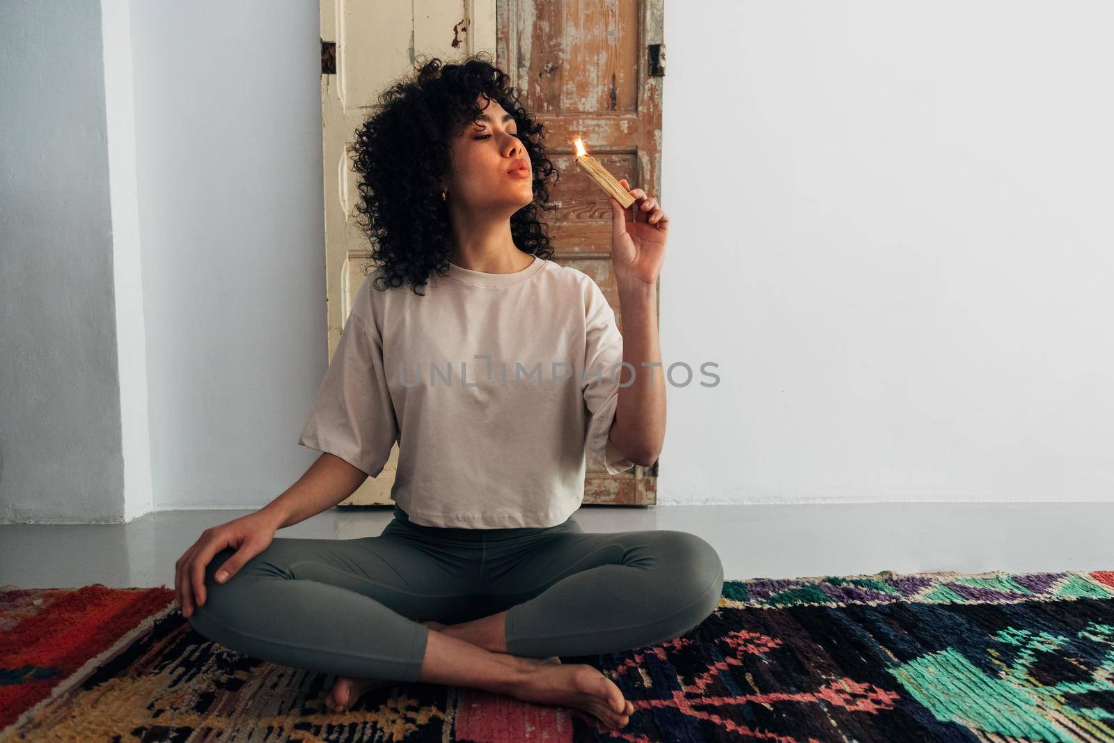 Young multiracial woman blowing flame of palo santo stick preparing to meditate. Copy space. by Hoverstock