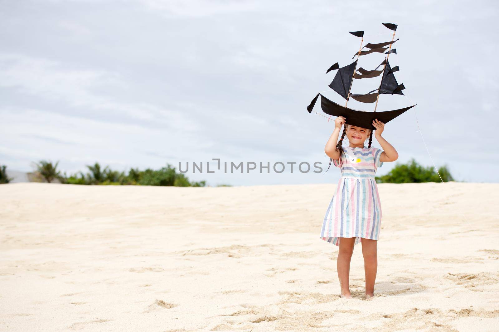 Cute little girl playing on the beach flying ship kite. Child enjoying summer family vacation at the sea.