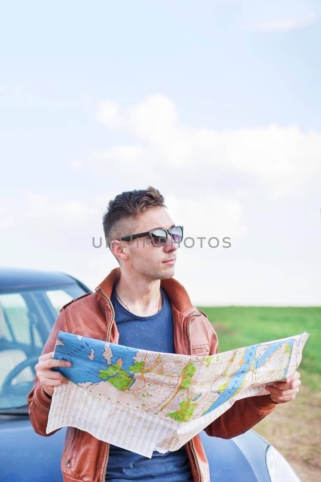 Young man reading road map near his car. lost track