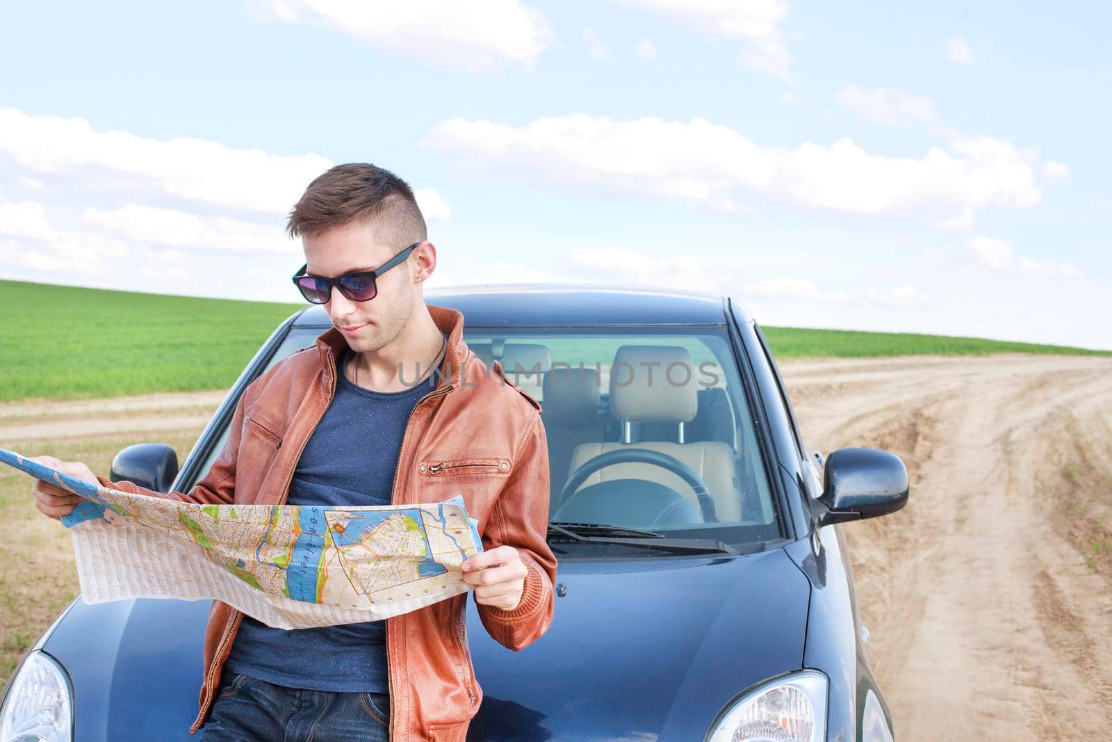 Young man reading road map near his car. lost track