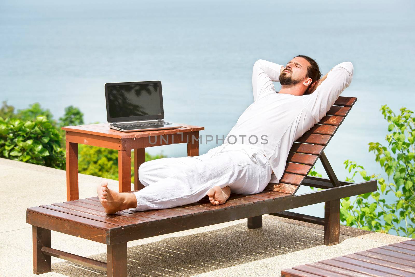 Businessman wearing white on deck chair typing laptop on the beach