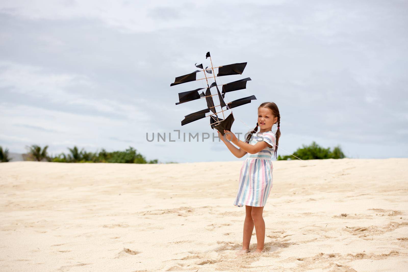 Cute little girl playing on the beach flying ship kite. Child enjoying summer family vacation at the sea.