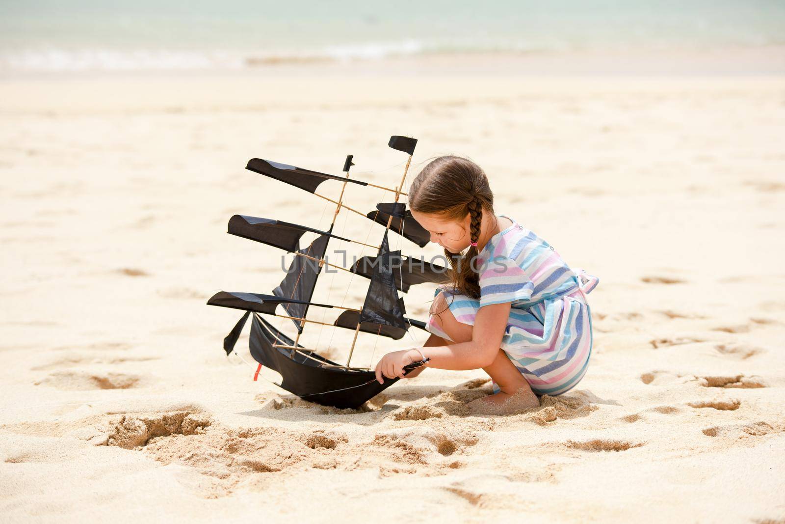 Girl playing on beach flying ship kite. Child enjoying summer. by Jyliana