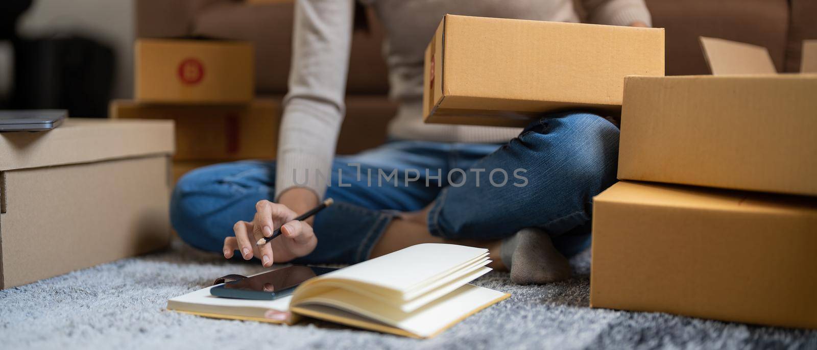 Close up businesswoman small stock business owner using phone and retail package parcel boxes checking commercial shipping delivery order