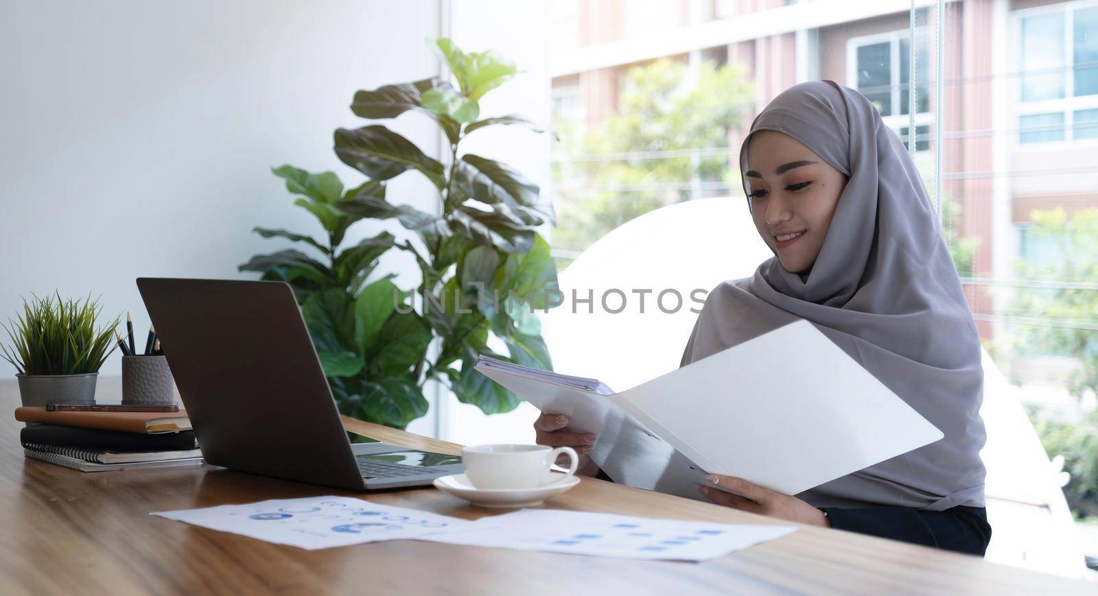 Portrait of Muslim Businesswoman Wearing Hijab Works on Project, Does Document Analysis. Empowered Digital Entrepreneur Works on e-Commerce Startup Project by wichayada