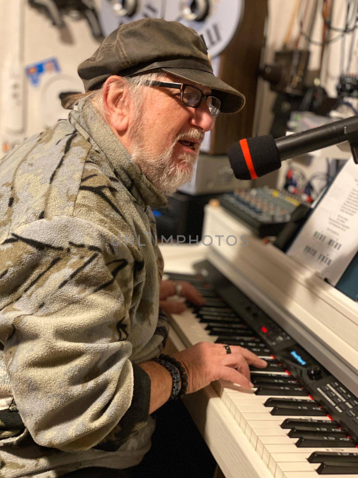 Senior singer sits behind a white piano and sings in a microphone.