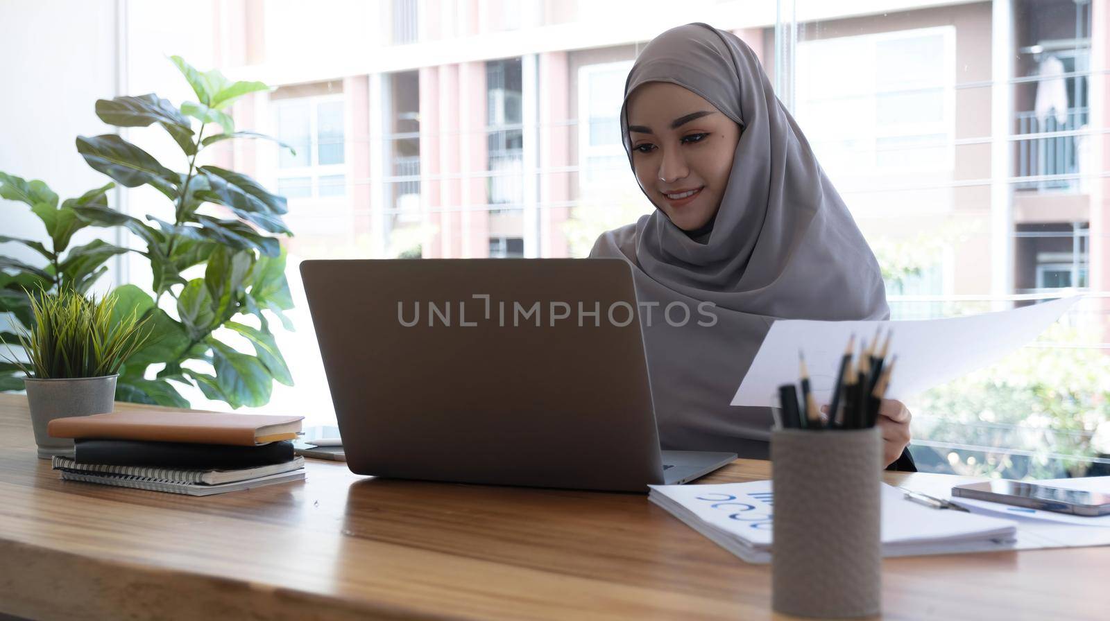 Portrait of Muslim Businesswoman Wearing Hijab Works on Project, Does Document Analysis. Empowered Digital Entrepreneur Works on e-Commerce Startup Project by wichayada