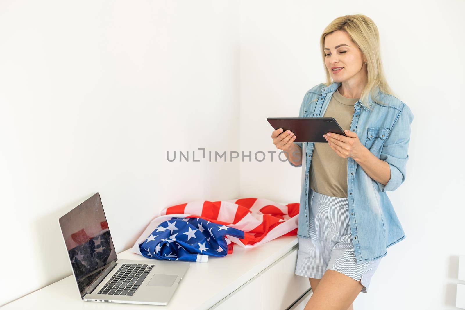 Happy woman employee sitting wrapped in USA flag, shouting for joy in office workplace, celebrating labor day or US Independence day. Indoor studio studio shot isolated on yellow background by Andelov13