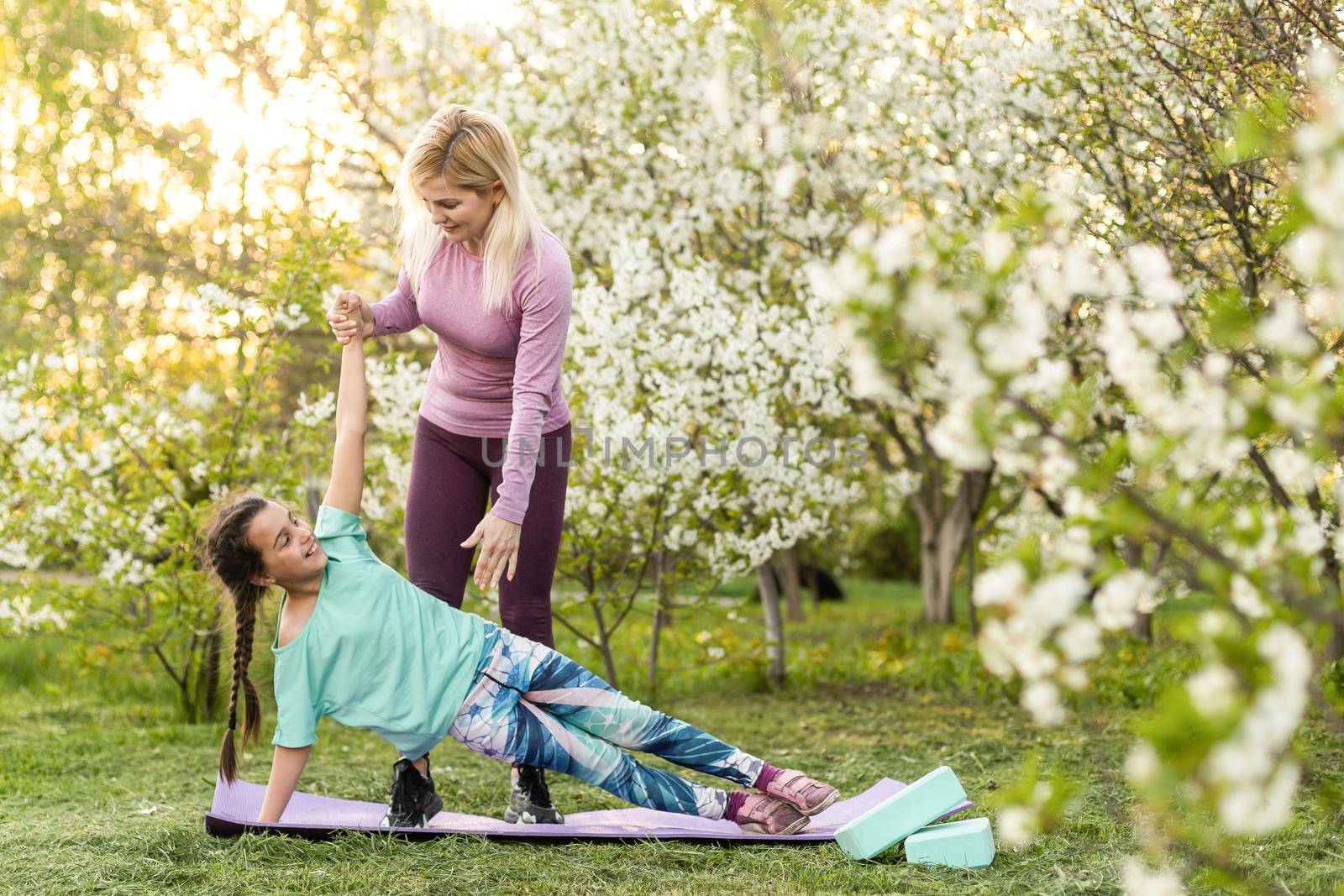 a young mother and daughter perform yoga exercises in the park on a gym mat. healthy lifestyle