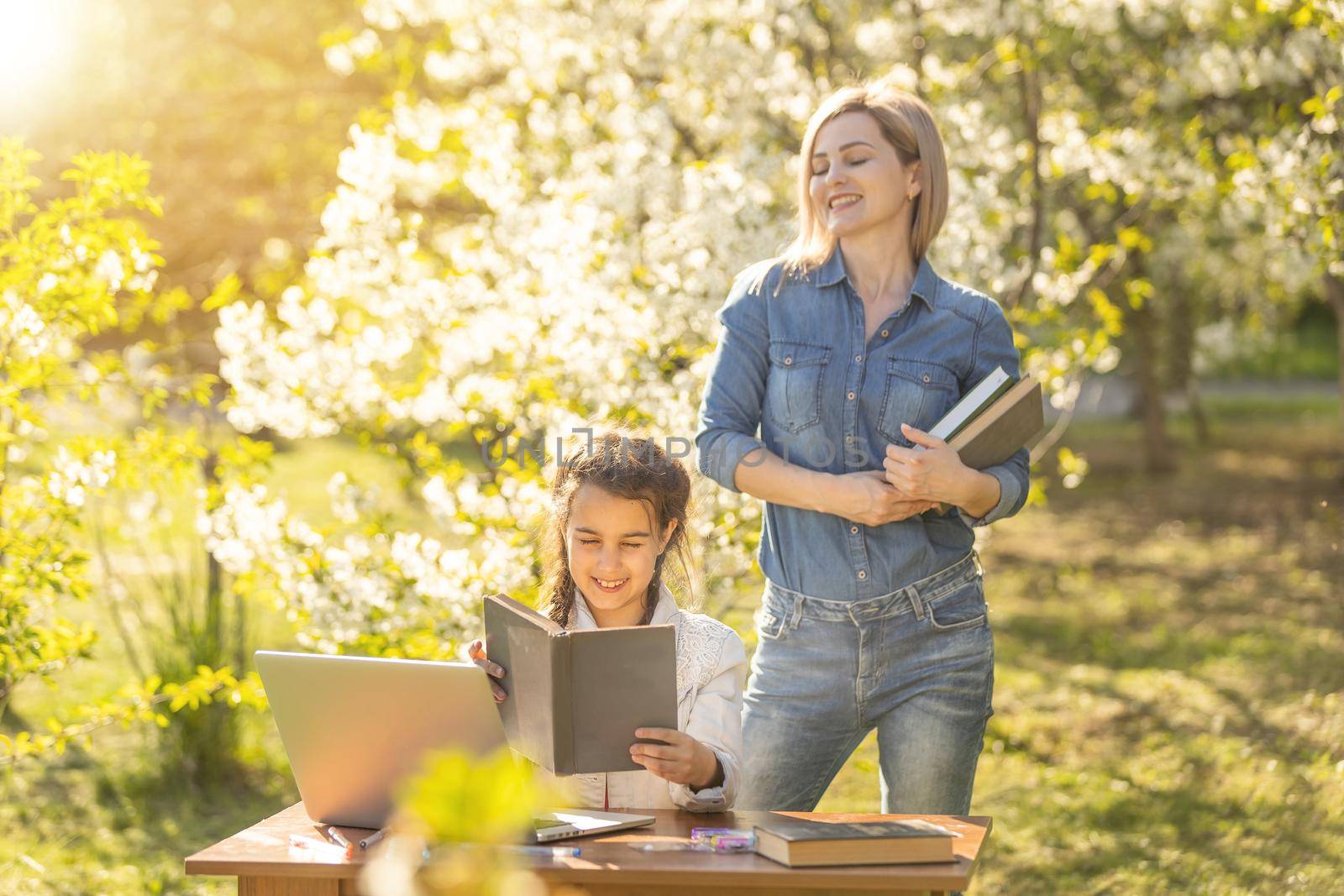 Mother helping her little daughter to use laptop computer. Child studying at home doing her homework or having online lesson. Homeschooling concept