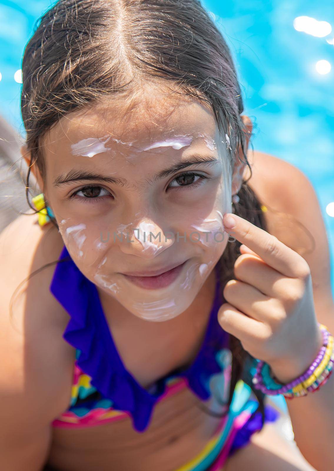 Child near the pool smears sunscreen. Selection focus. by yanadjana