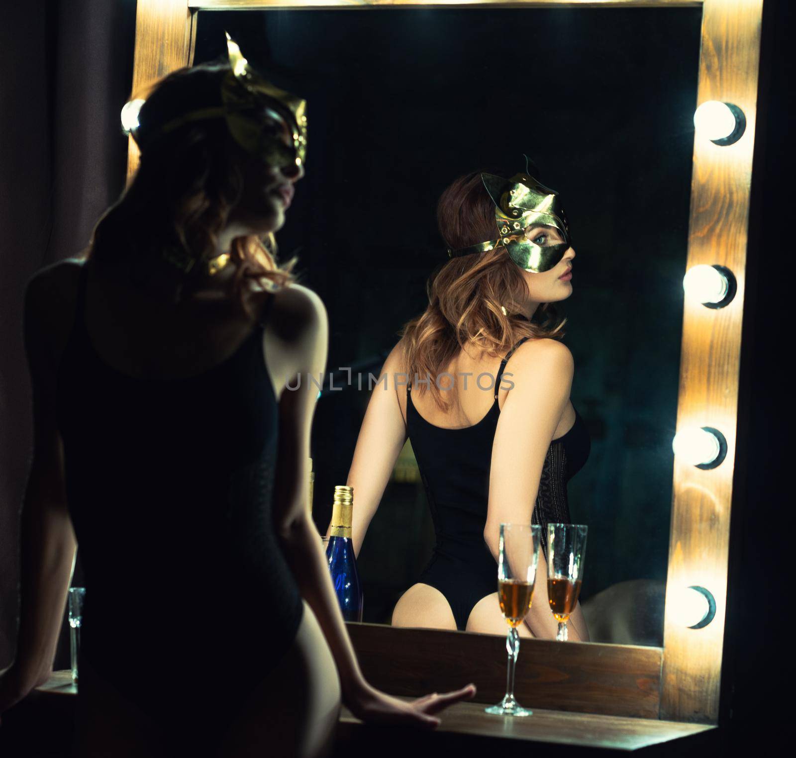 Silhouette with reflection of passionate girl in mask, black body lingerie posing next to the make up mirror. Girl in sexy underwear. Shot of sexy woman in black lingerie at home. Toned image.