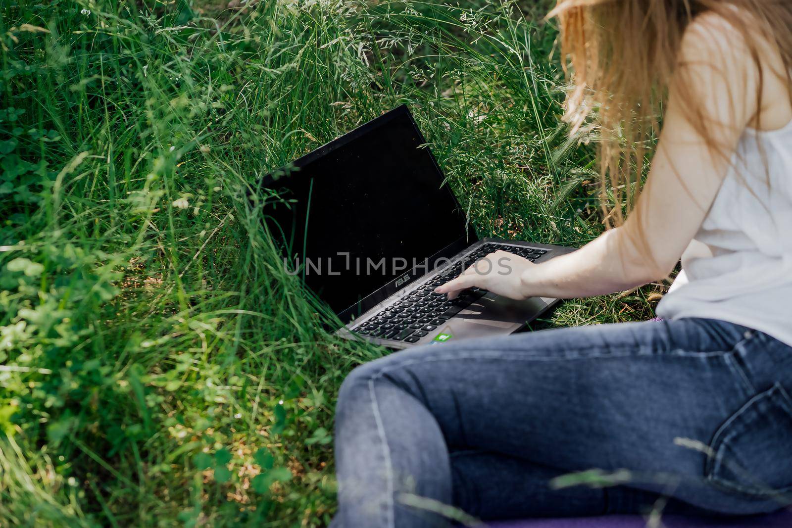 girl sits on the grass and works at a laptop. freelance. selfeducation. the concept of distance learning outdoors. by Anyatachka