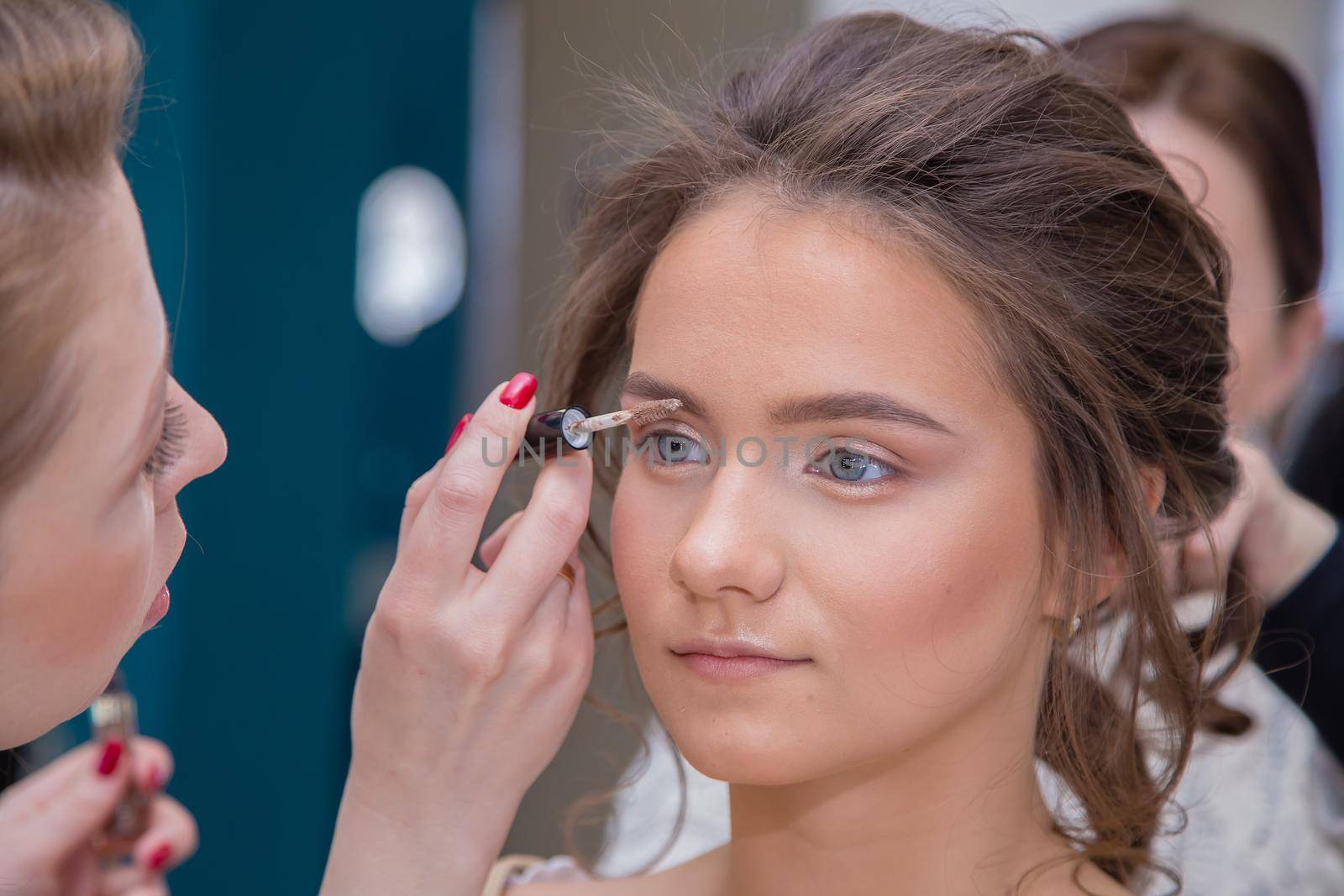 Make-up artist with a brush paints the eyebrows close-up of a girl. Female master makes makeup to a young woman. Business concept - beauty salon, facial skin care, cosmetology.