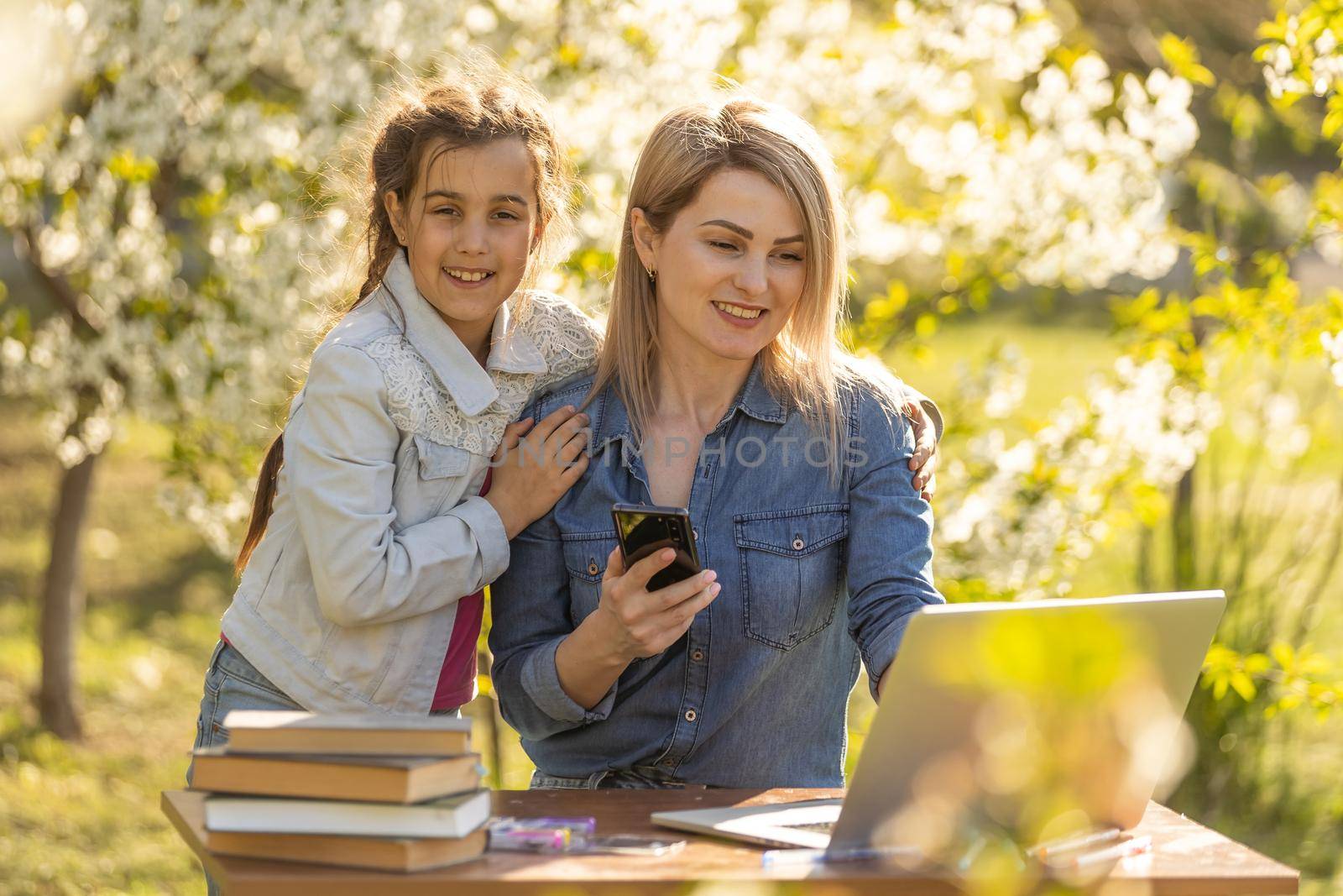 Mother helping her little daughter to use laptop computer. Child studying at home doing her homework or having online lesson. Homeschooling concept