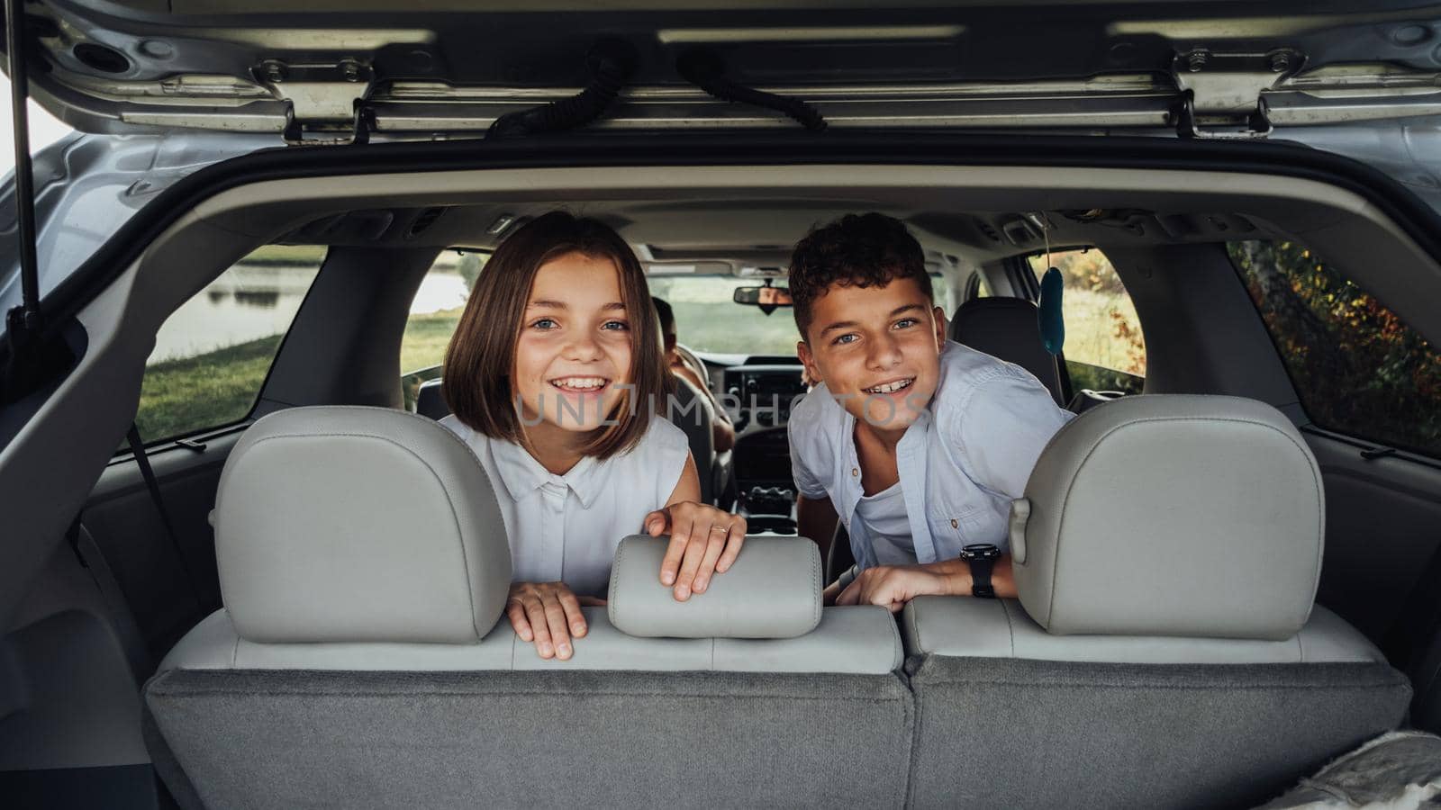 Young Girl and Boy Looking Out of Trunk of Minivan Car, Cheerful Teenage Children Enjoying Weekend Road Trip with Parents