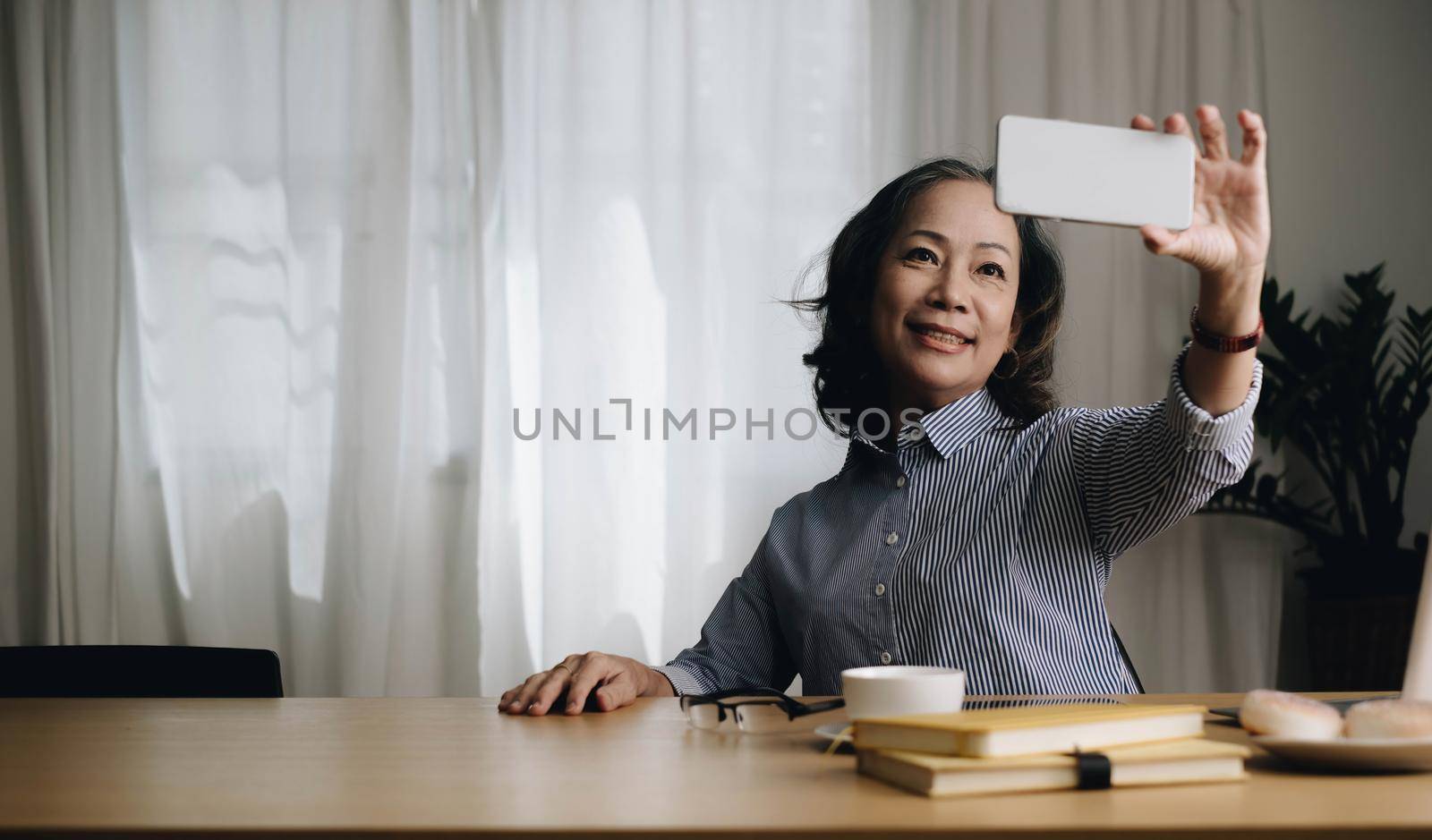 Asian senior elderly woman smile and video call in living room at home. Strong elderly older grandmother feeling happy using mobile cell phone communicate with family enjoy retirement life in house. by wichayada