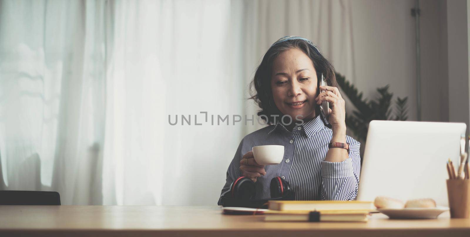 Happy pretty mature woman speaking on mobile phone portrait. Senior grey haired lady making telephone call, sitting on couch at home, enjoying talk, communication by wichayada