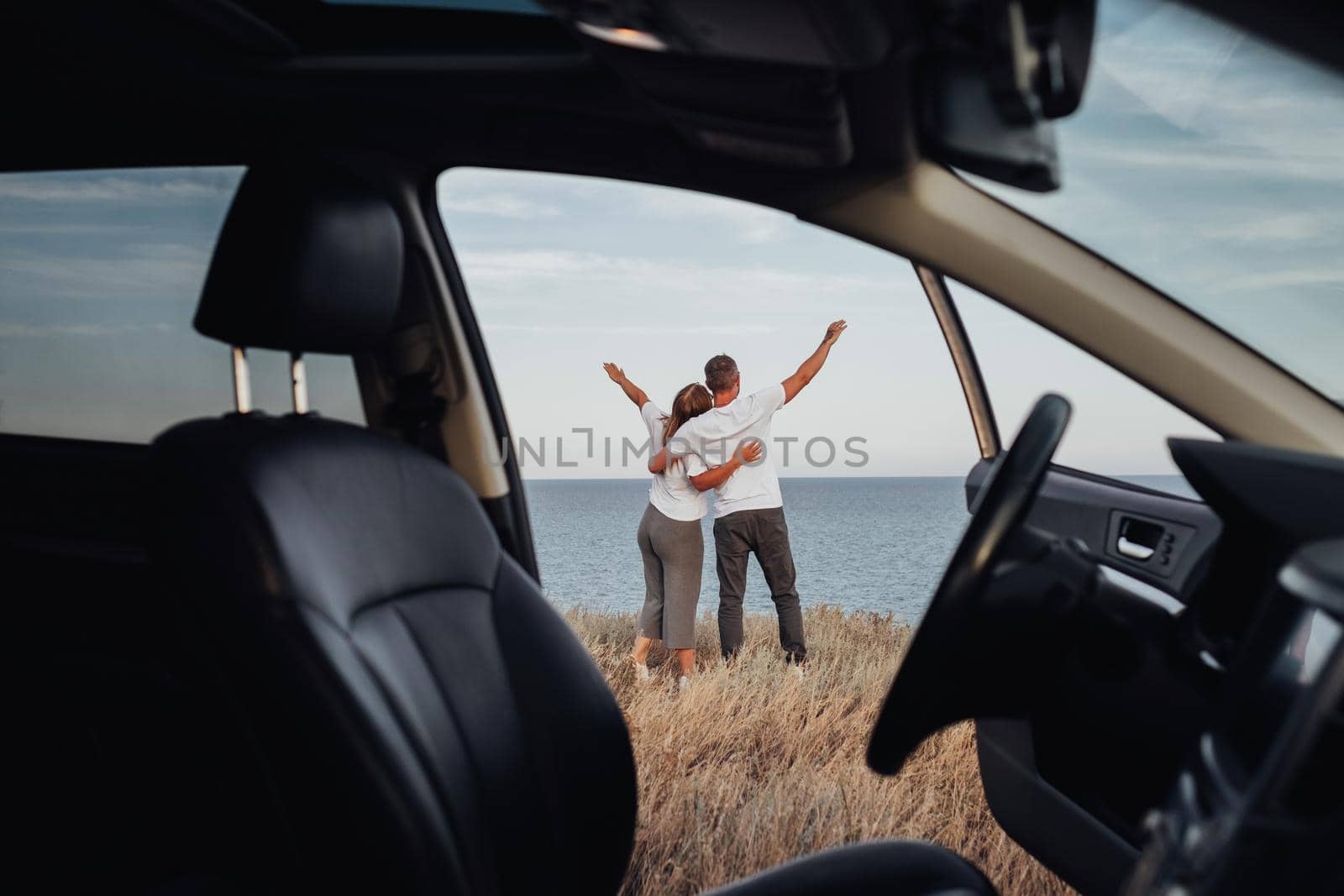 View From Car Interior, Young Couple on a Road Trip, Man and Woman Embracing on Sea Background by Romvy