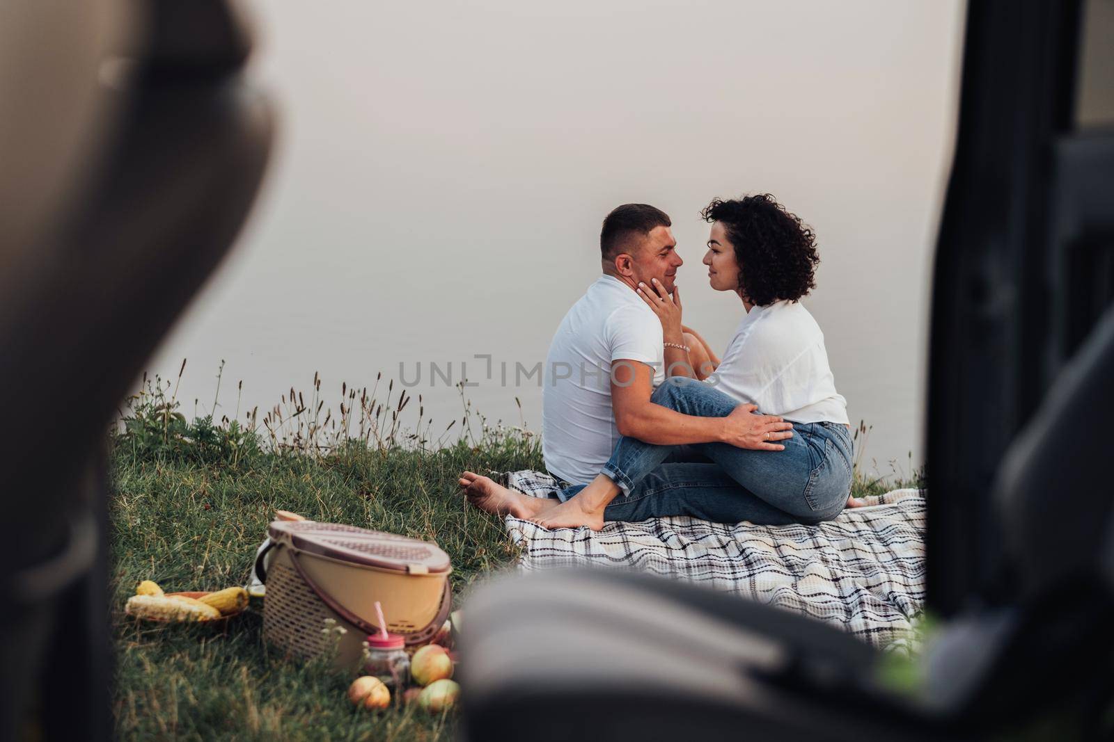 View From Car Happy Middle Aged Couple Having Picnic Outdoors, Man and Woman on a Romantic Weekend by Lake at Sunset