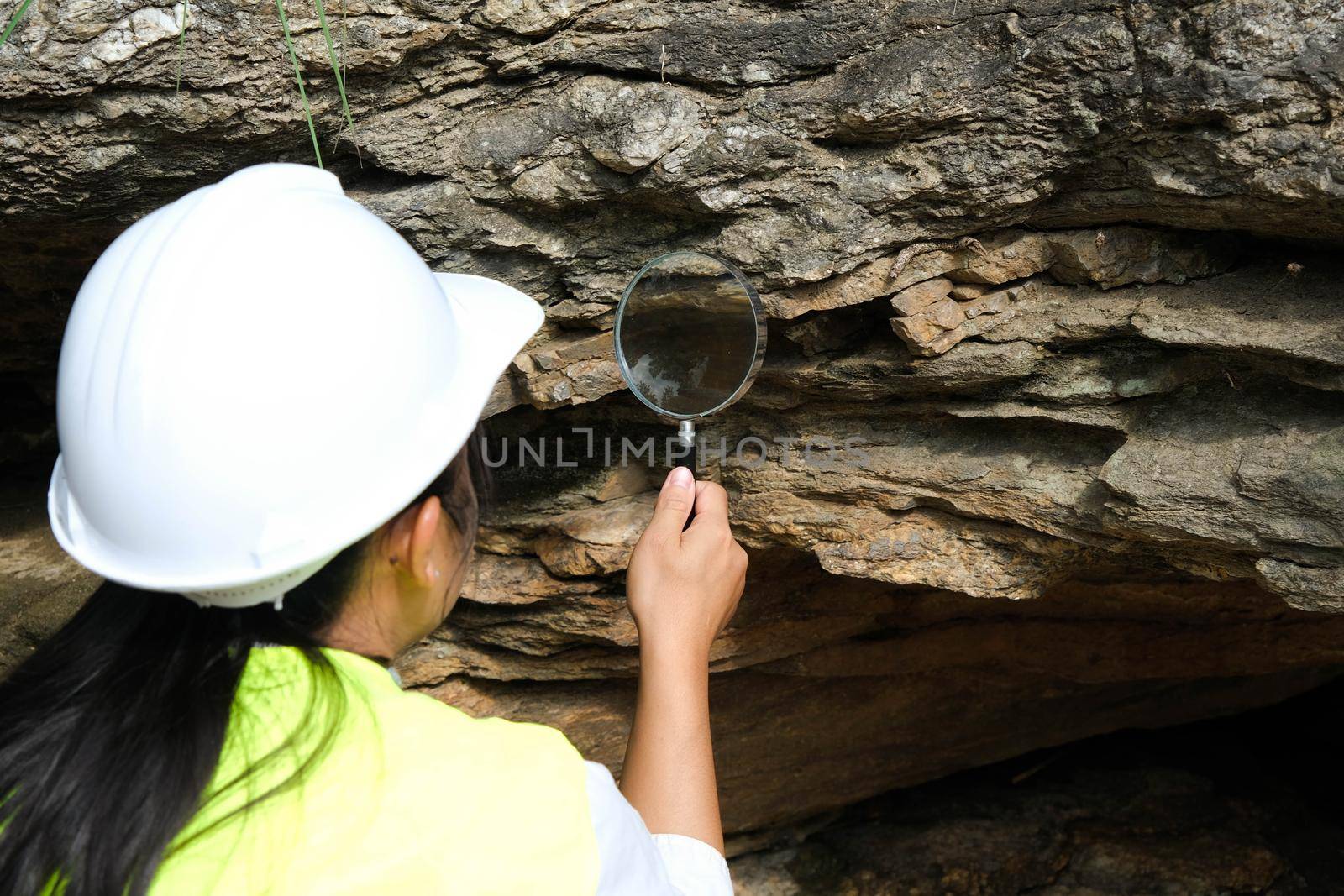 Asian female geologist researcher analyzing rocks with a magnifying glass in a natural park. Exploration Geologist in the Field. Stone and ecology concept.