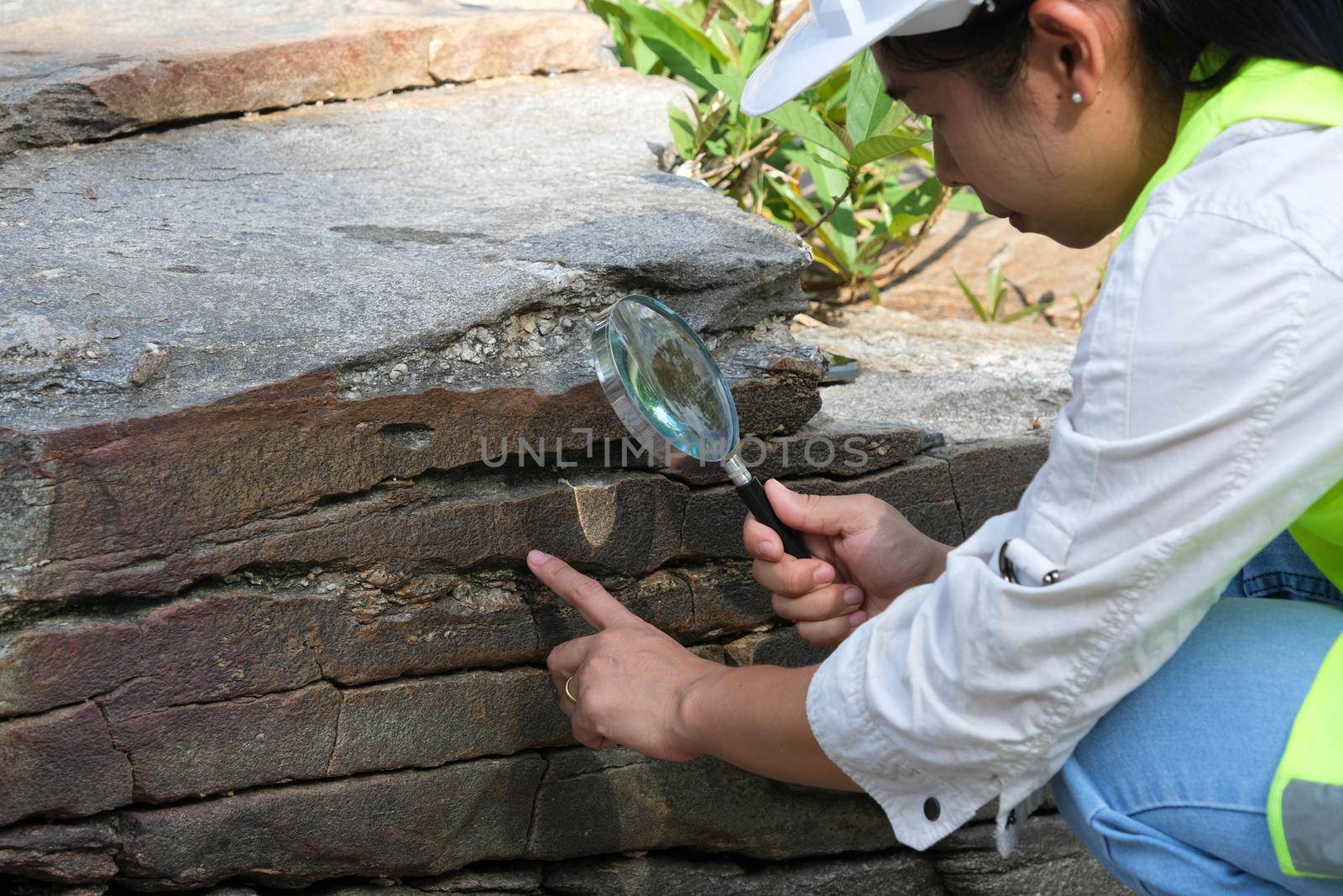 Asian female geologist researcher analyzing rocks with a magnifying glass in a natural park. Exploration Geologist in the Field. Stone and ecology concept.