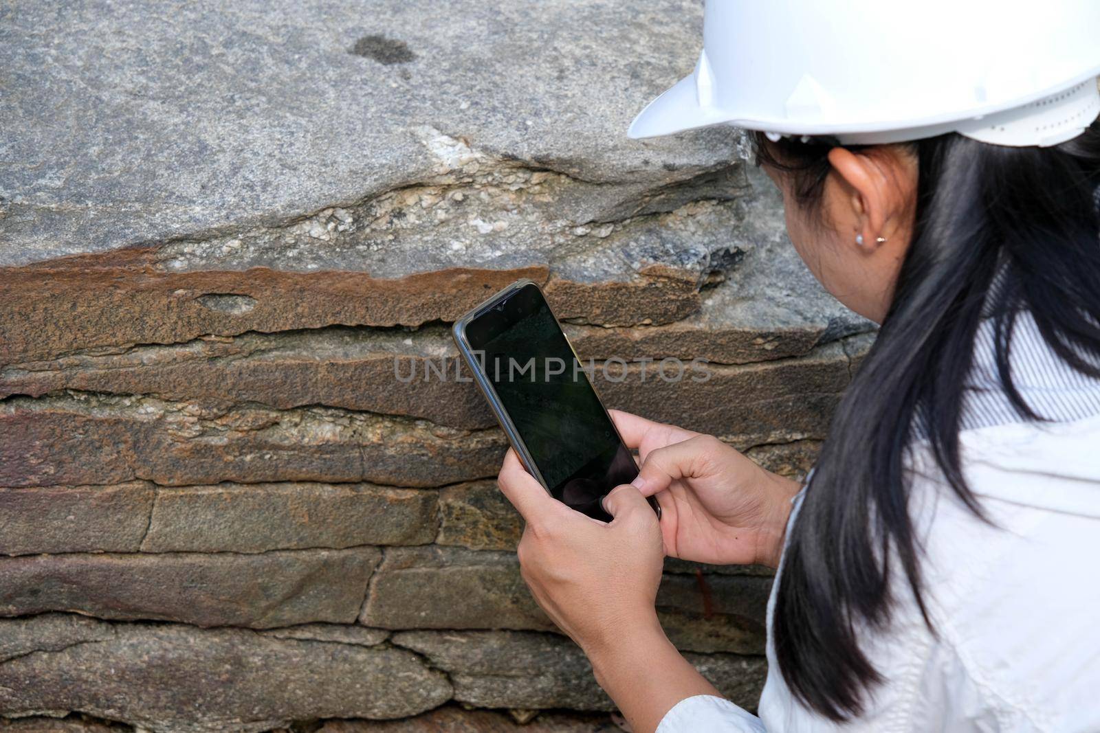 Asian female geologist researcher is analyzing rocks with a smartphone in a natural park. Exploration Geologist in the Field. Stone and ecology concept.