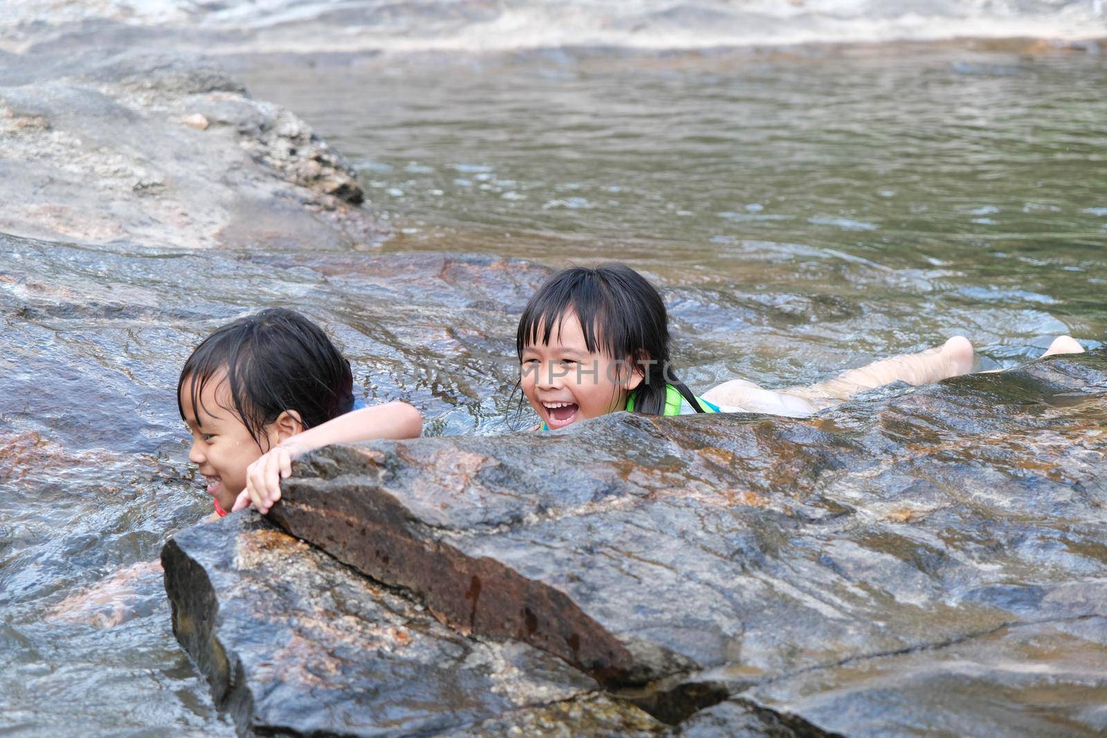 Cute Asian children wearing life jackets are enjoying playing in the river. Two little sisters enjoyed swimming in the stream. Healthy Summer Activities for Kids.