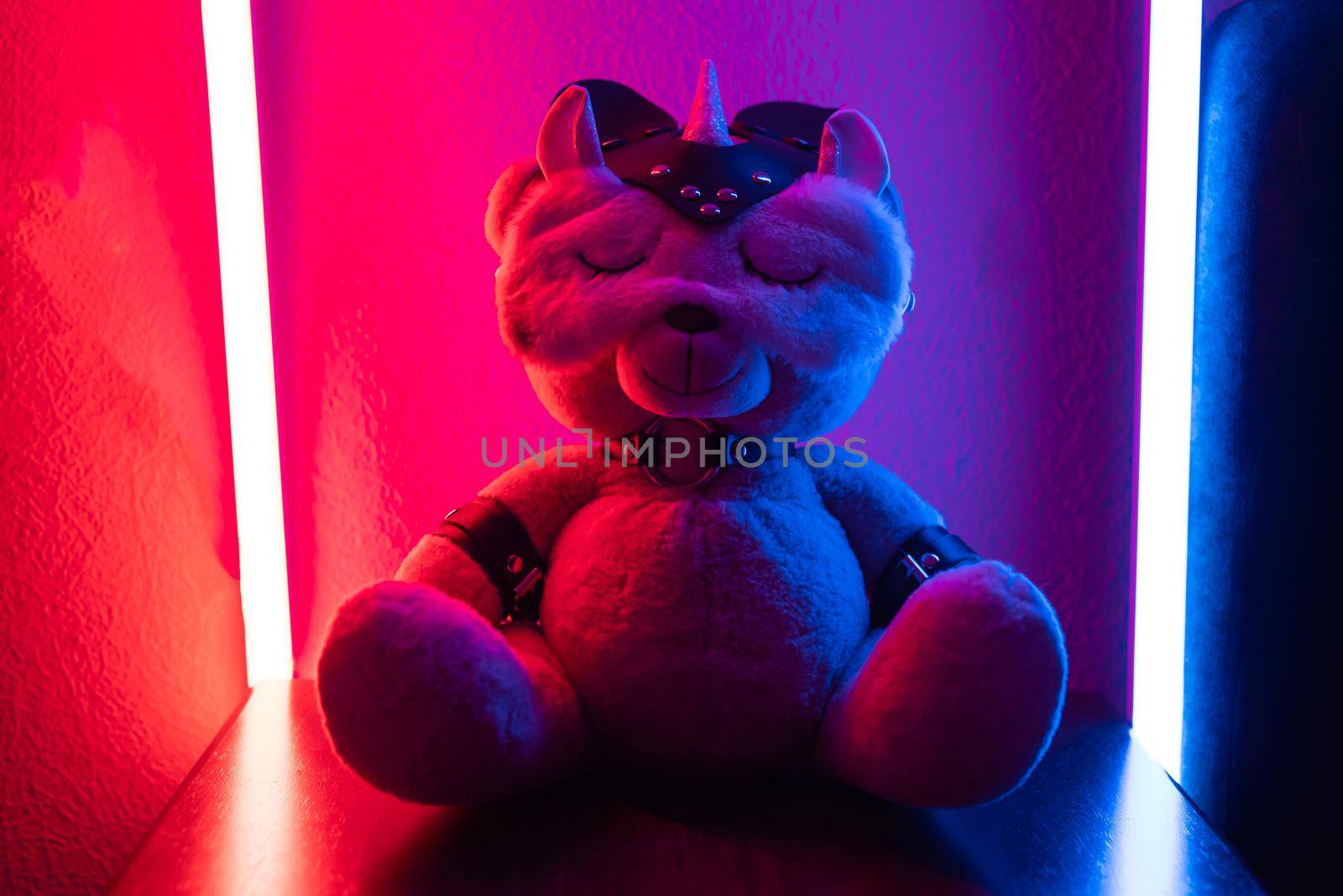 the toy teddy bear dressed in leather straps and a mask, an accessory for BDSM games in a sleep mask