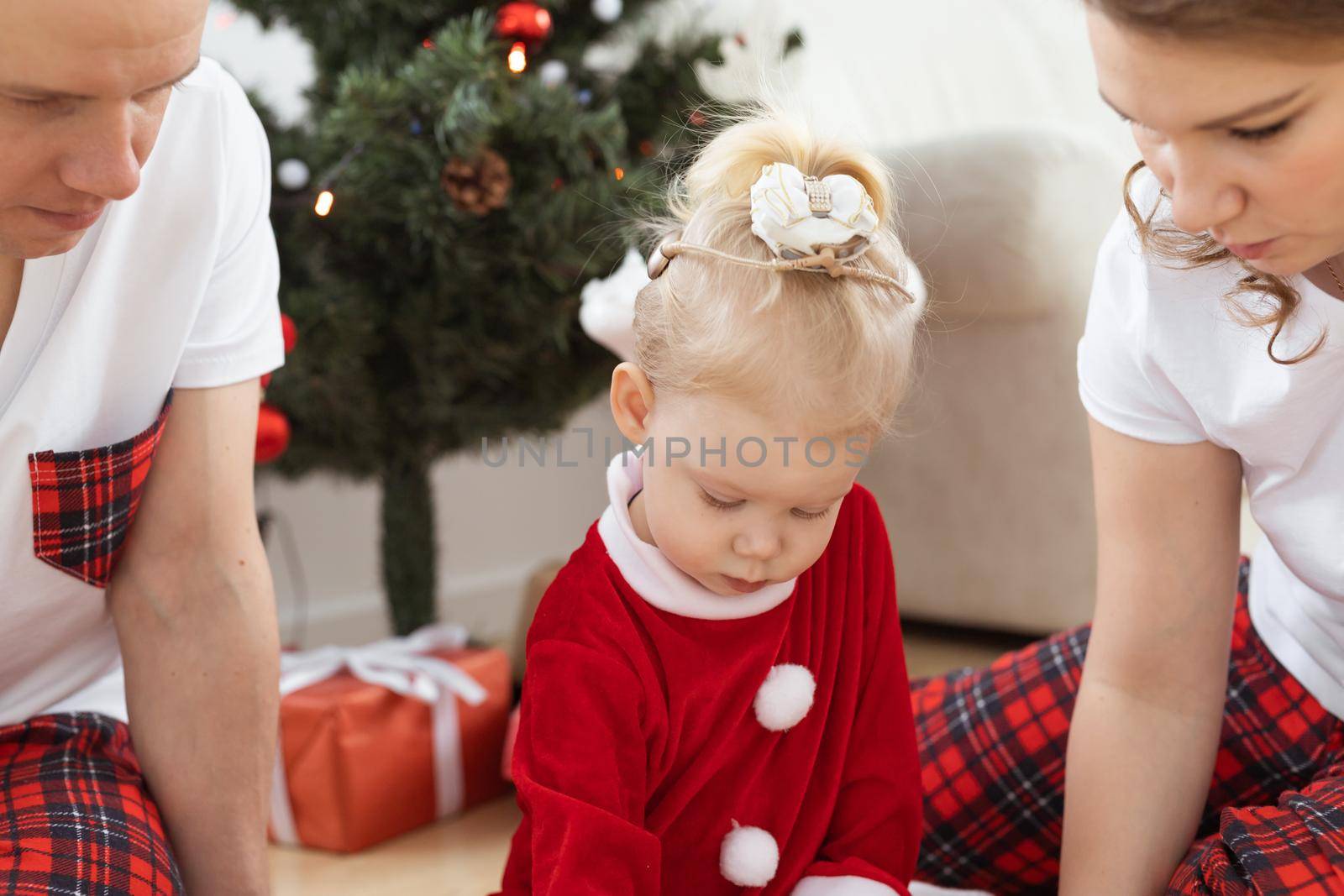 Toddler child with cochlear implant plays with parents under christmas tree - deafness and innovating medical technologies for hearing aid and diversity by Satura86