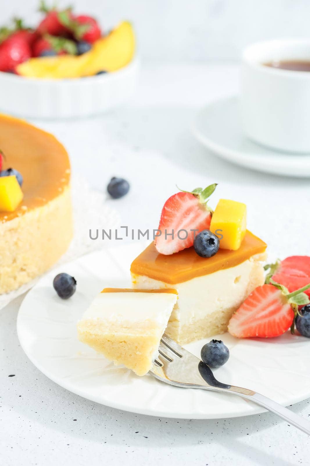 A piece of cheesecake with mango on a plate with a tea fork decorated with berries and flowers on a gray background. Healthy food.