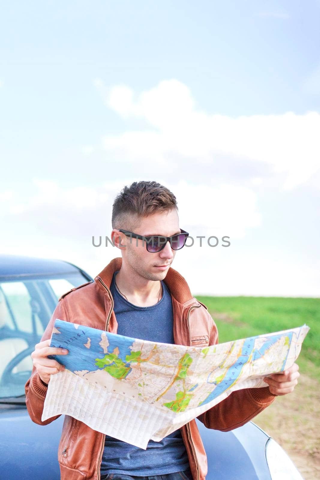 Young man reading road map near his car. lost track