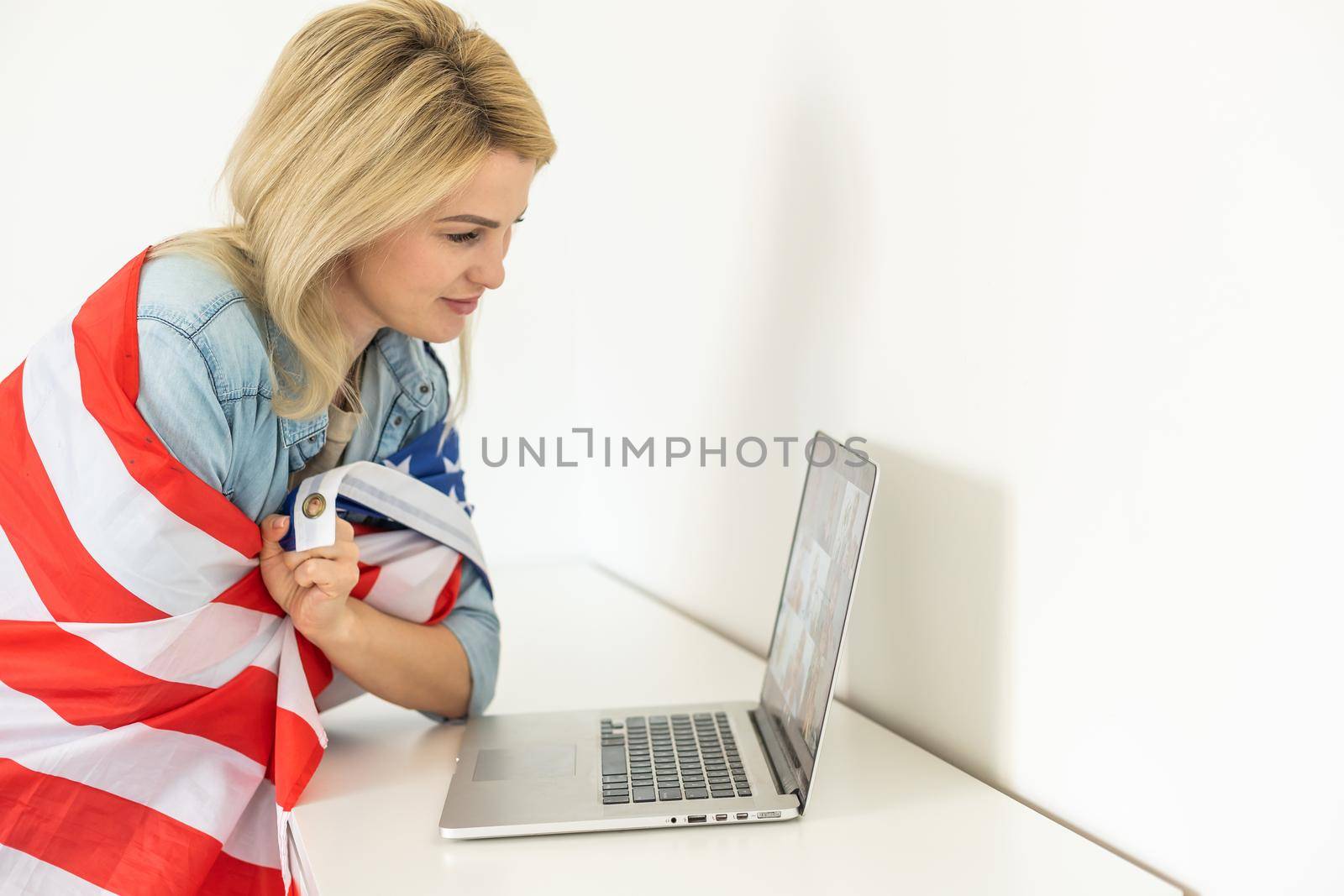 Happy woman employee sitting wrapped in USA flag, shouting for joy in office workplace, celebrating labor day or US Independence day. Indoor studio studio shot isolated on yellow background by Andelov13