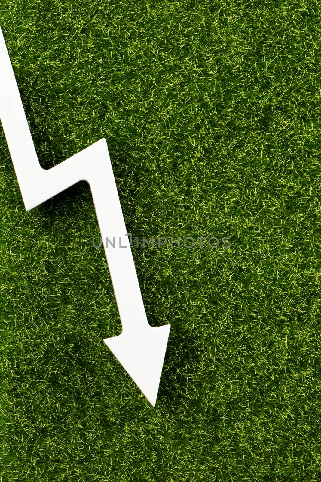 White chart arrow on green grass pointing down. Business loss symbol, ecology concept, green energy spending. by SERSOL