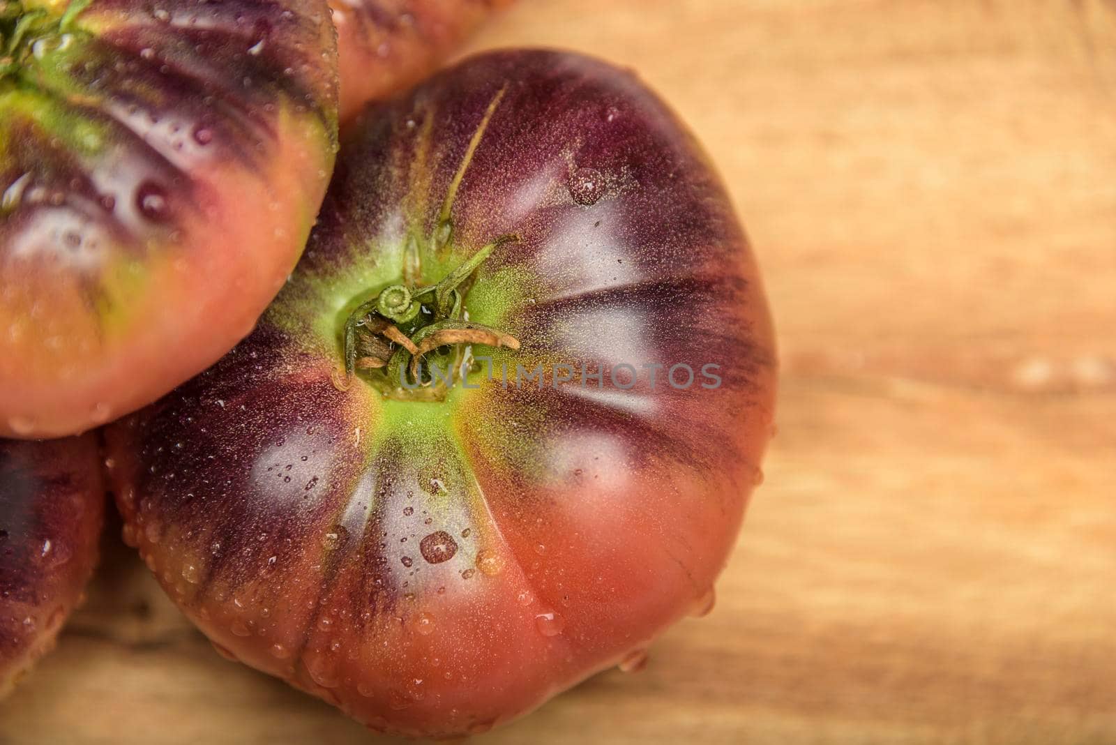 Tiger tomato on a cutting board with basil leaves on wooden background. Copy space. Fresh tomato wased for cooking. Tomato with droplets of water